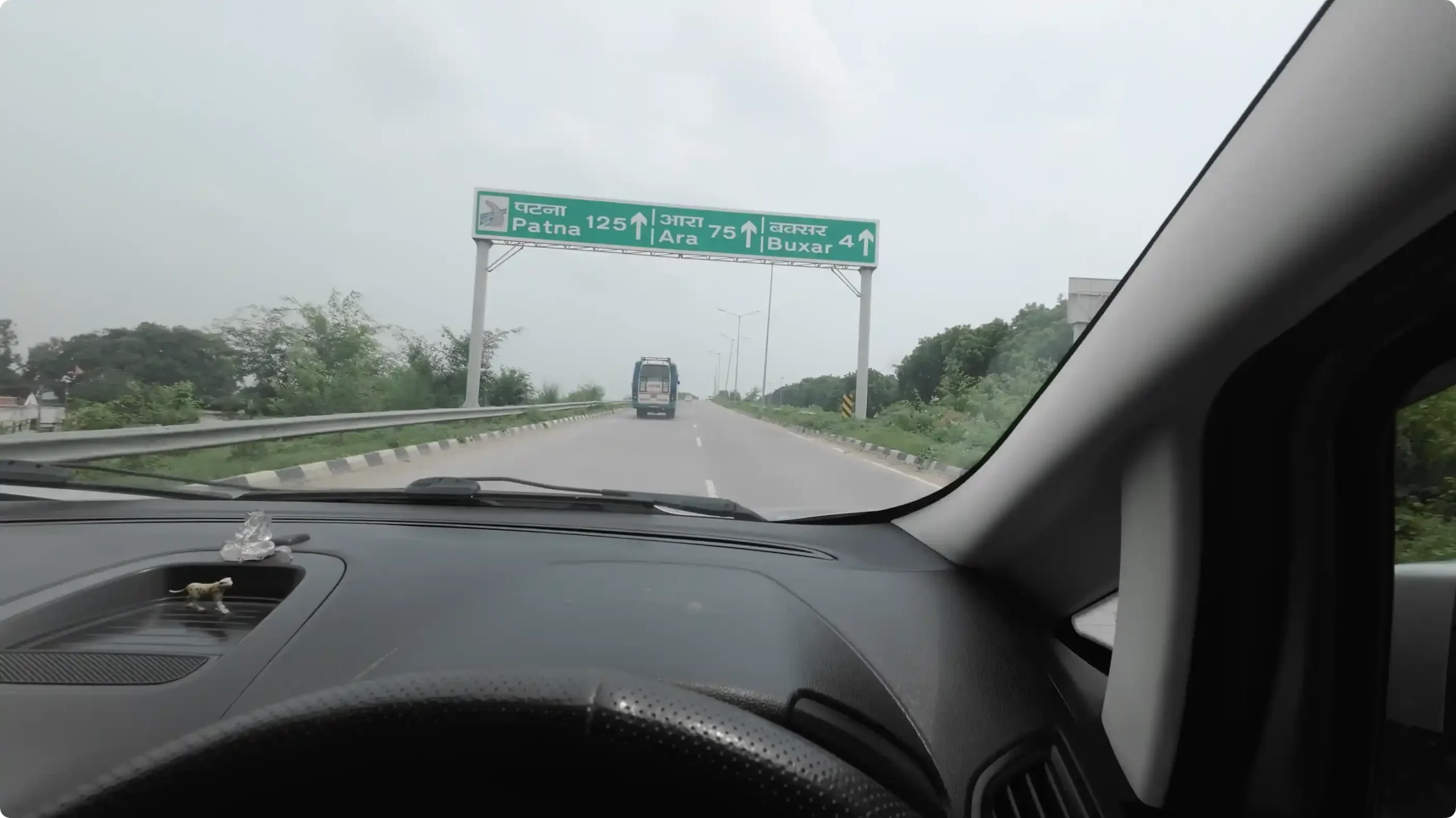 A car dashboard view showing a green overhead highway distance board indicating Patna is 125 km away